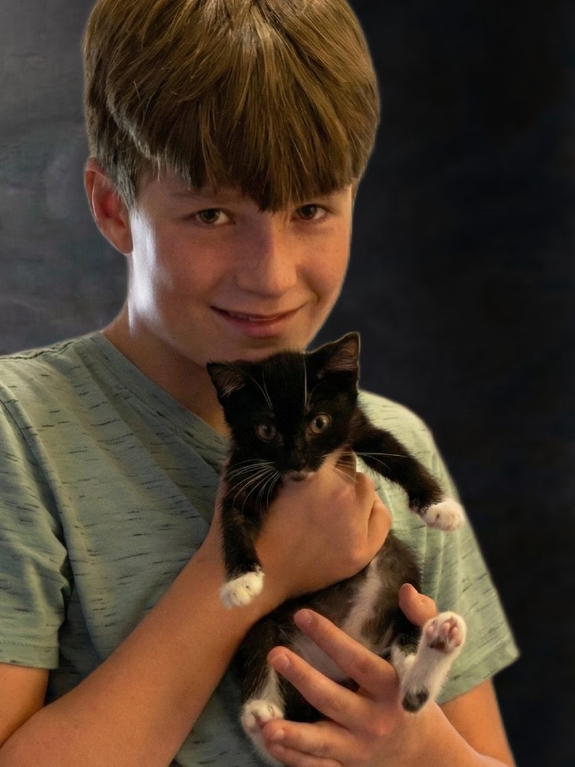 A smiling boy from the Maxi’s Multi family gently holding a black-and-white kitten